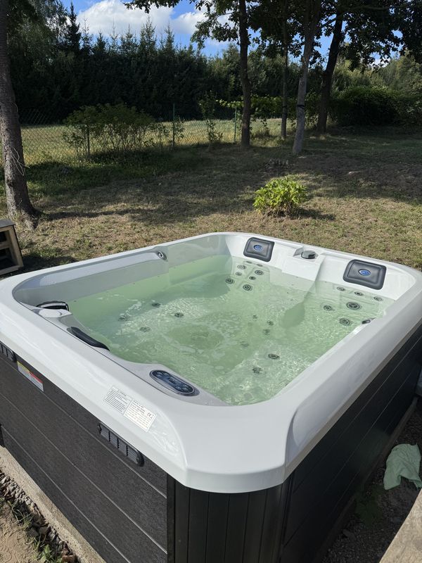 Jacuzzi Pablitto z białą wanną i ciemną obudową na betonowej płycie w ogrodzie