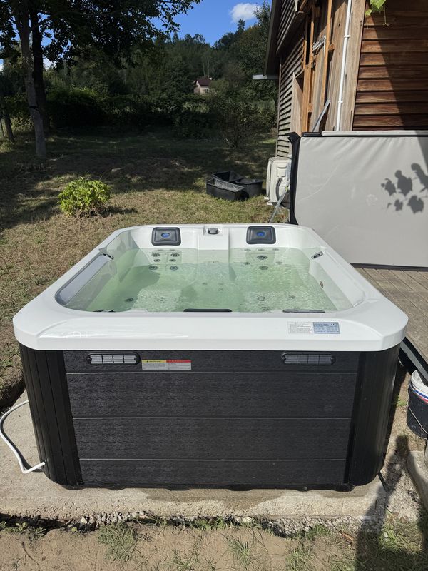 Jacuzzi Pablitto od przodu, obok drewniany dom i pokrywa termiczna