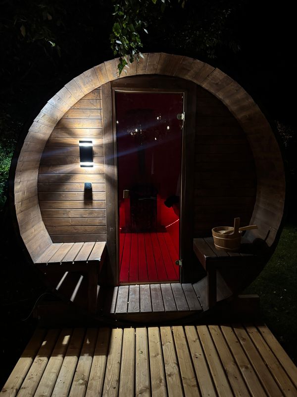 Sauna Beczka wieczorem: otwarty przedsionek z ławkami i podświetlone drzwi