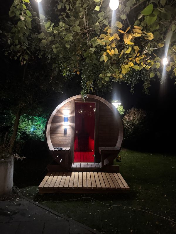 Sauna Beczka nocą w ogrodzie, na drewnianym podeście